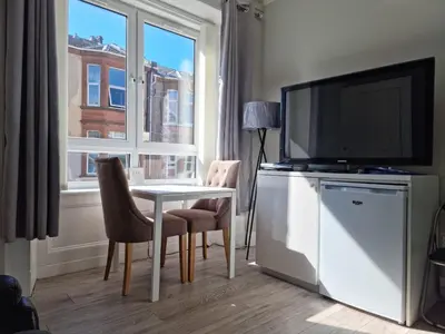 a living room with a table and a tv and a window at Carrick - One Bed Apartment in Largs