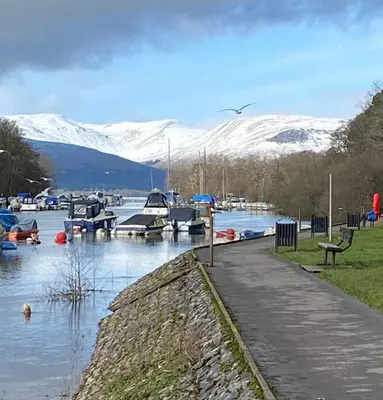 a marina with boats in the water with snow covered mountains at Riverside View Apartment in Balloch, Loch Lomond in Balloch