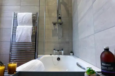 a bathroom with a tub with a shower and towels at Airds Apartments in Oban
