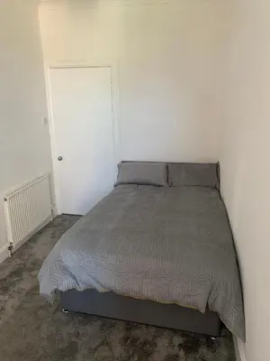 a bed in a bedroom with a white wall at Woodvale Flat, Renton, Loch Lomond in Renton