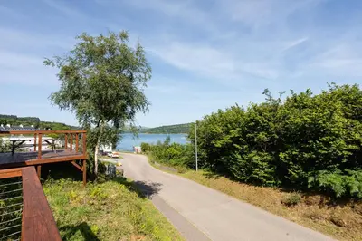 a path next to a lake with a wooden bridge at Highland Basecamp in Lochaline