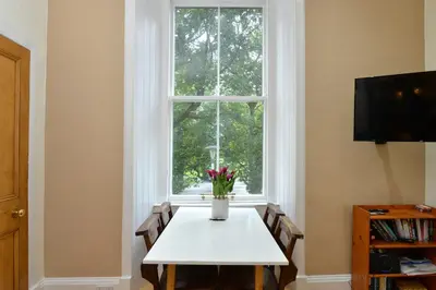 a table with a vase of flowers sitting in front of a window at Home by The Meadows, close to City Centre in Edinburgh