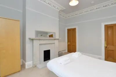 a white bedroom with two beds and a fireplace at Home by The Meadows, close to City Centre in Edinburgh