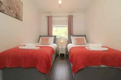 a room with two beds with red blankets and a window at Signature - Culzean House in Newarthill