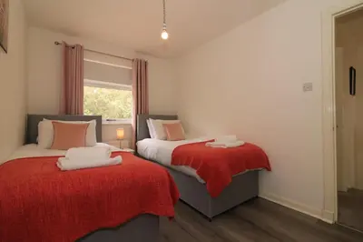 a bedroom with two beds with red blankets and a window at Signature - Culzean House in Newarthill