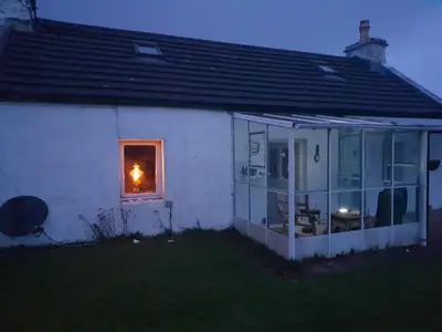 a small white house with a candle in a window at Tigh Na Maraiche in Isle of Jura