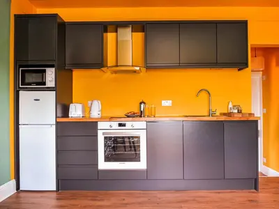a kitchen with black cabinets and an orange wall at Holst Apartment in Newton Stewart