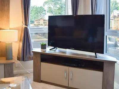 a flat screen tv on a wooden stand in a living room at Riverside Lodge in Auchterarder