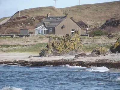 a house on a beach next to the water at Shore Cottage in Bellochantuy
