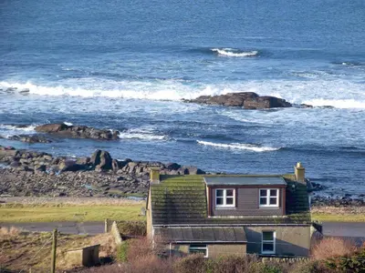 a house with a green roof sitting next to the ocean at Shore Cottage in Bellochantuy