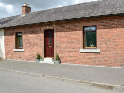a brick building with two windows and two potted plants at Lime Tree Cottage in Drumpark
