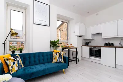 a living room with a blue couch and a kitchen at Cheerful 2 Bedroom Homely Apartment, Sleeps 4 Guest Comfy, 3x Double Bed, Parking, Free WiFi, Suitable For Business, Leisure Guest,Glasgow, Glasgow West End, Near City Centre, Perfect For Common Wealth Games 2026 in Glasgow