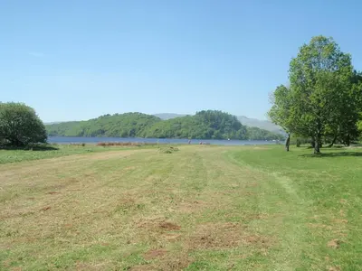 a field of grass next to a body of water at Loch Lomond Waterfront Luxury Lodges in Balmaha