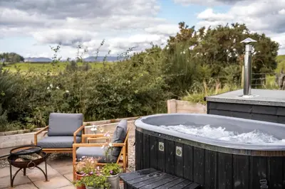 a jacuzzi tub on a patio with a chair at Luxury Glamping Pods - The Heft & The Hirsel in Glasgow
