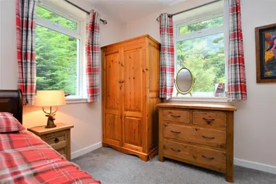 a bedroom with a wooden dresser and two windows at Nursery Cottage Benmore in Benmore