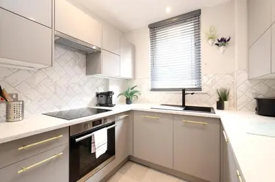 a white kitchen with white cabinets and a window at JOIVY Modern 1 bed Flat in West End, close to Princes Gardens in Edinburgh