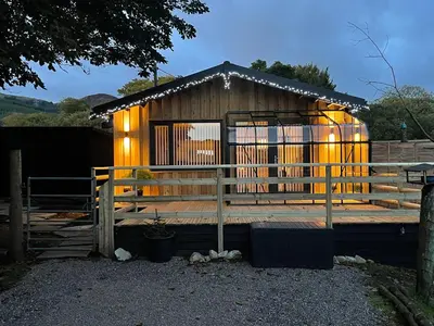 a small wooden building with a porch and a fence at Spacious lodge with king sized bed in Inveraray