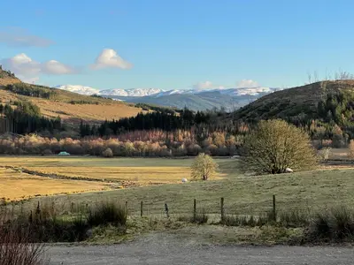 a field with a fence and mountains in the background at Spacious lodge with king sized bed in Inveraray