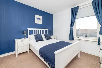a blue bedroom with a white bed and a window at Balmoral Residence 30 mins from Edinburgh and Glasgow in Falkirk