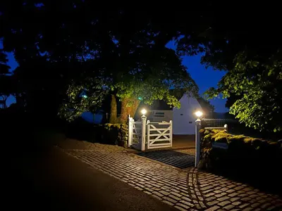 a white gate with a fence and a tree at night at Whitehouse in Uplawmoor