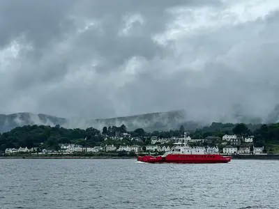 a red boat in the water with a town in the background at Dunoon River Clyde Flat in Innellan