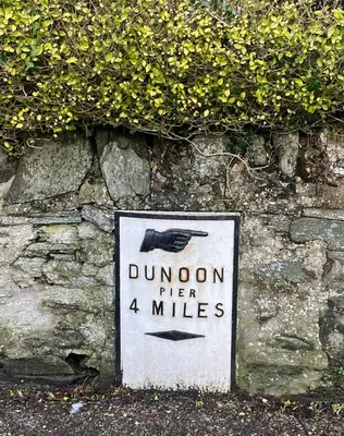 a sign for dunoon after miles on a stone wall at Dunoon River Clyde Flat in Innellan