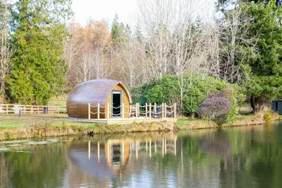 a large wooden dome house next to a body of water at The Secret Hideaway in Penicuik
