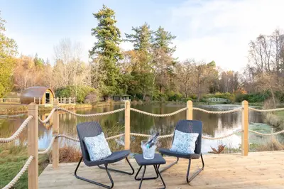 two chairs sitting on a wooden deck next to a pond at The Secret Hideaway in Penicuik