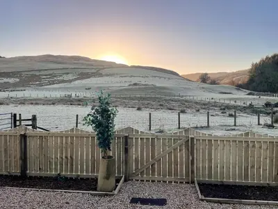a fence with a tree in front of a field at Mossdale Cottage in Dalmellington