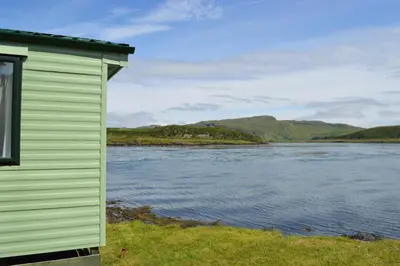 a green building next to a body of water at Sunnybrae, Isle of Luing in Cullipool