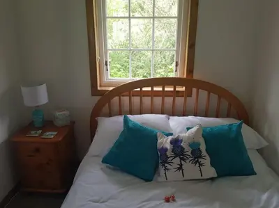 a bed with blue and white pillows and a window at Pine Cabin, Strathyre. A cosy escape from it all. in Strathyre