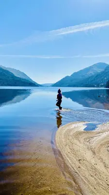 a person is standing on the shore of a body of water at Luxurious mountain retreat lodge Hunters Quay in Dunoon