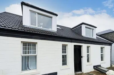 a white house with a black roof at Cross Road Apartment in Paisley