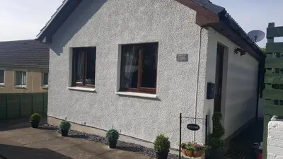 a white house with two windows and potted plants at Machrie Cottage, Oban, in Oban