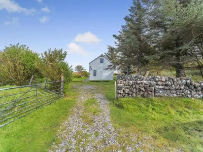 a stone fence and a white house in the background at The Bothy - Uk37414 in Bunessan