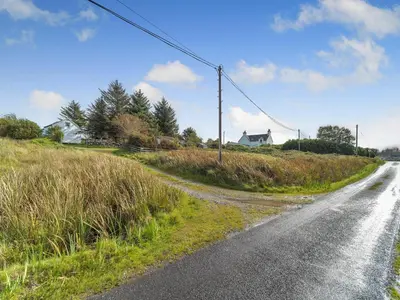 an empty road in a field with houses in the background at The Bothy - Uk37414 in Bunessan