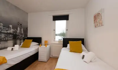 two beds in a room with white walls and yellow pillows at PREMIER - Chapel House with Driveway! in Cleland