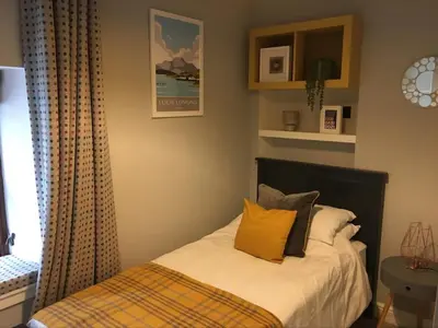 a bed with yellow pillows in a bedroom at Roselea Cottage in Luss