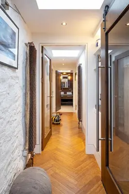 a hallway with white walls and wood floors and a door at Roselea Cottage in Luss