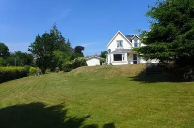 a white house on top of a grassy hill at Allandale House in Brodick