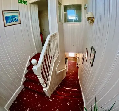 a stairway with red carpeting and a white staircase at Allandale House in Brodick