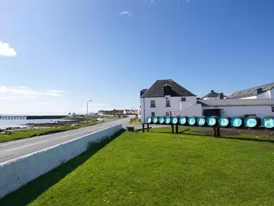 a road next to a building and a beach at Burnside Cottage in Bruichladdich