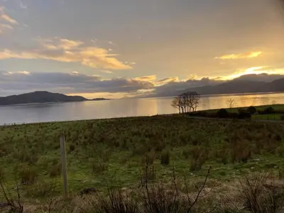 a field with a tree in the middle of a lake at Springbank Apartment - Sleeps 4 - Pet Friendly in Fort William