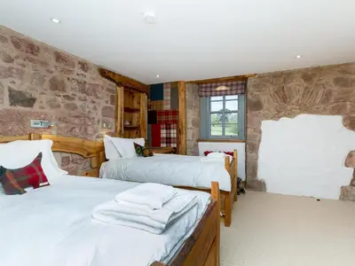 a bedroom with two beds and a stone wall at Knock Old Castle in Largs