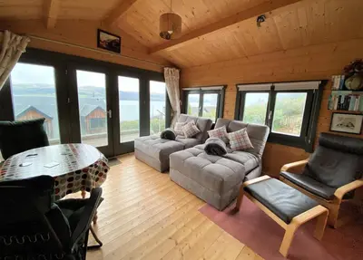 a living room with a couch and a table and windows at The Neuk in Tighnabruaich
