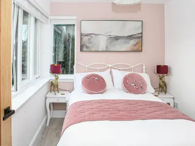 a bedroom with a bed with pink walls and windows at Forget Me Not Cottage in Culross