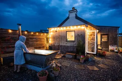 a woman in a bath tub in front of a house at Jura, Mrs Leonard's Cottage in Isle of Jura