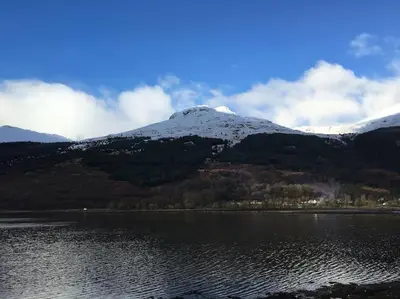 a mountain with snow on top of it next to a lake at Viking Cottage in Arrochar