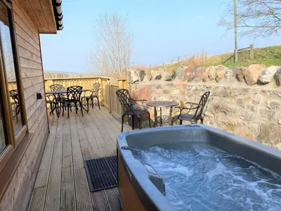 a hot tub on a deck with a table and chairs at Partridge Lodge with Hot Tub in Forgandenny