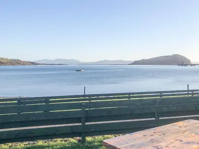 a bench next to a lake with a boat in the water at Gleaner Lea Apartment in Campbeltown